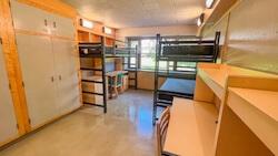Residence hall room with three beds, two closets, a dresser, and three desks. 