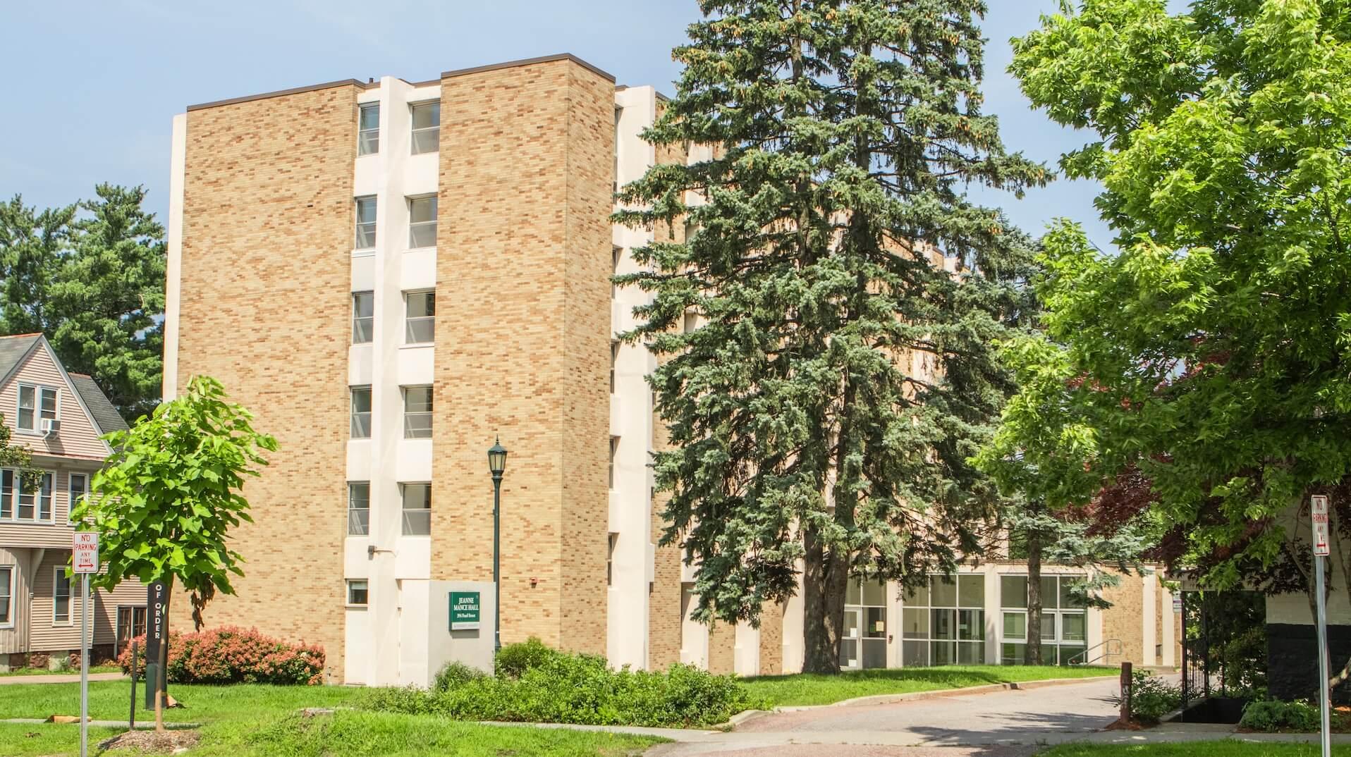 A six-story brick and concrete residence hall with trees beside it. 