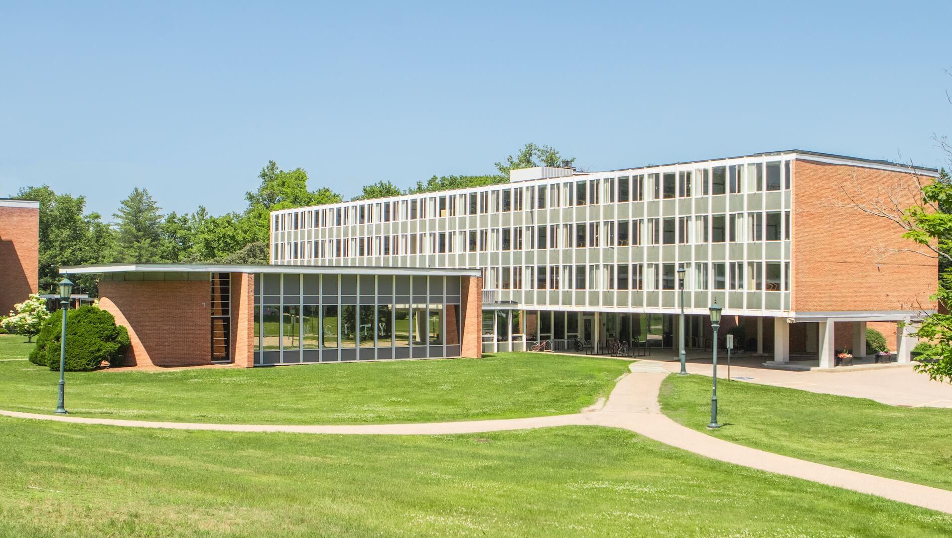 A four-story brick residence hall with a large wall of windows next to a grassy area. 