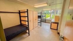 A room with two beds, two dressers, and two desks.