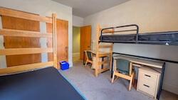 A room with two beds, two dressers/closets, and two desks.