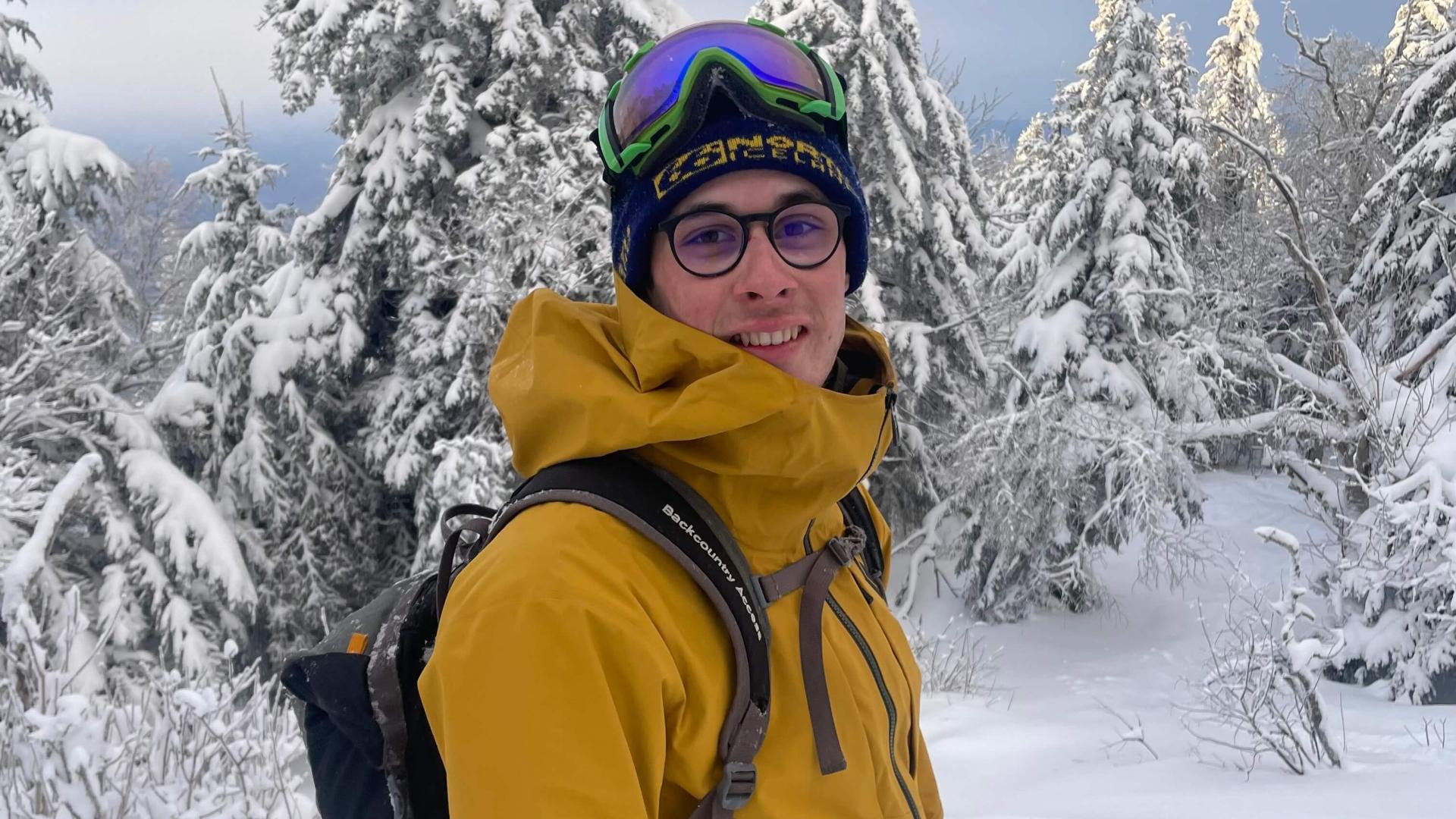 Finn in ski gear standing in front of snowy trees.