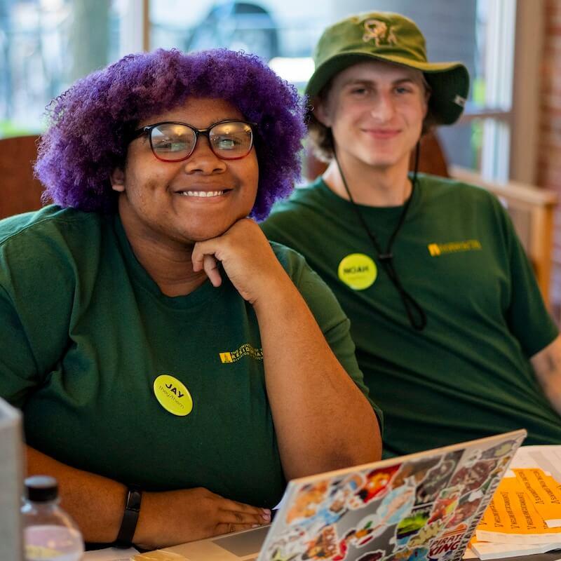 Two students smiling in green UVM uniform t-shirts. 