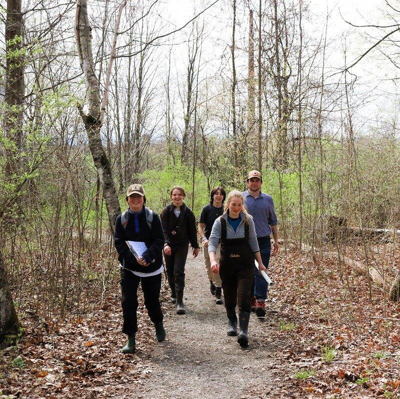 Five students outside walking along a trail, smiling and dressed for outdoor field work