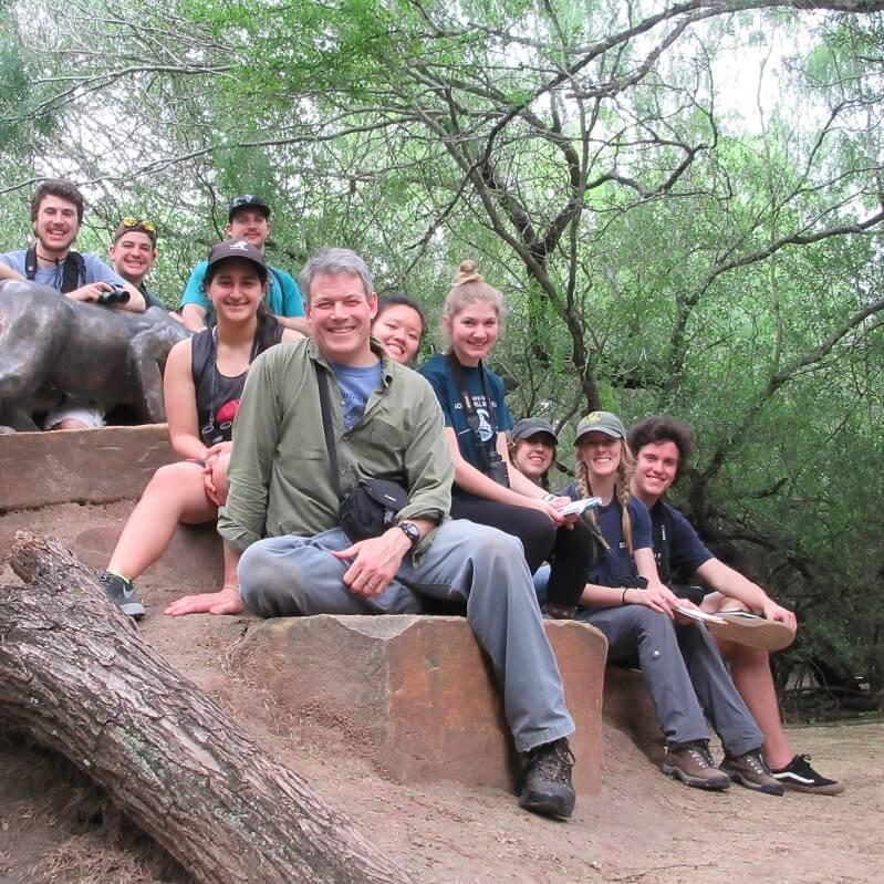 Professor Allan Strong and a group of students on a travel trip in Texas, sitting on a rocky ledge outside.